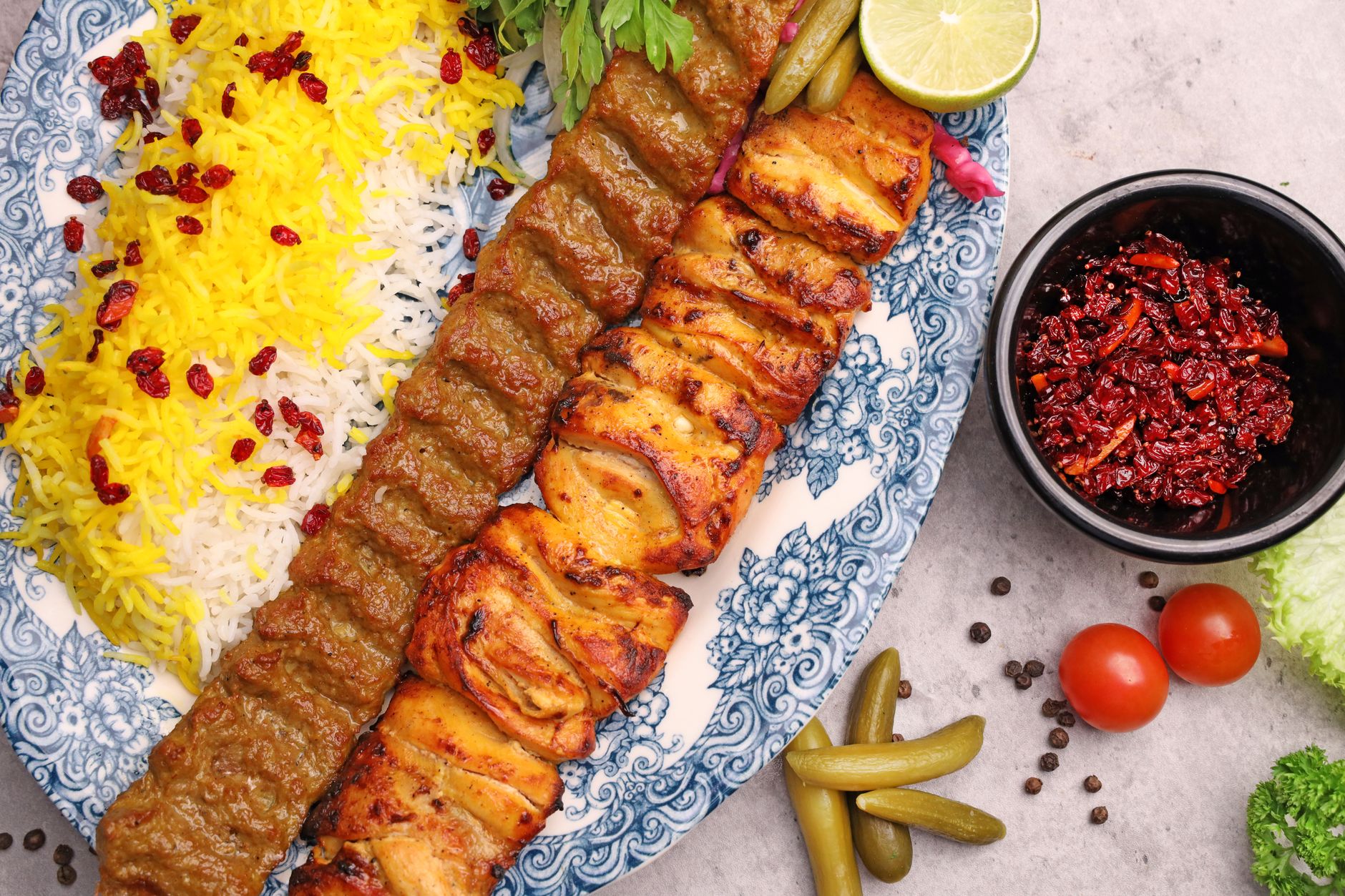 A platter of charcoal-grilled kebab beside saffron-tinted basmati rice and grilled tomato